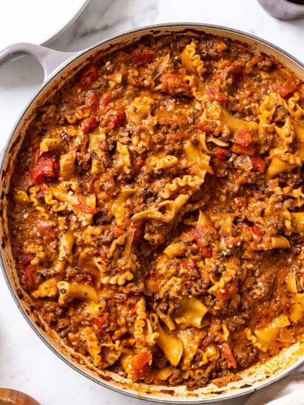 Large pot filled with cooked weeknight ragù with pasta and pieces of tomato all on marble surface with glass on red wine to the side.