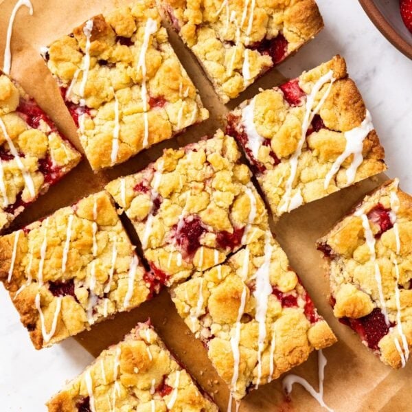 White marble surface with strawberry crumb bars cut into pieces and drizzled with white glaze over the top.