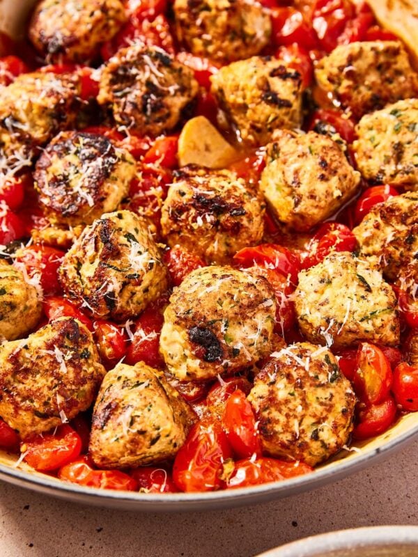 Large skillet filled with chicken zucchini meatballs nestled in tomato sauce with burst grape tomatoes and pieces of garlic after cooking.