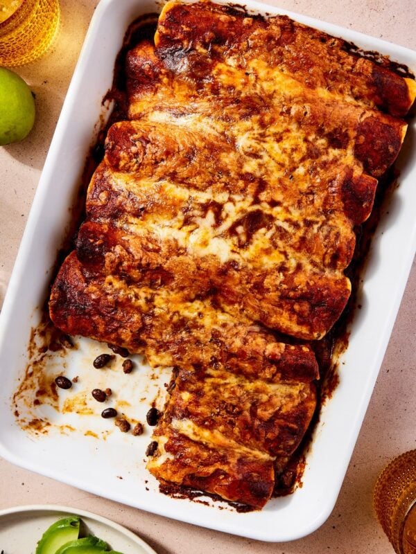 Rectangular white baking dish filled with baked beef enchiladas with cheese all over the top and two tortillas partially missing.