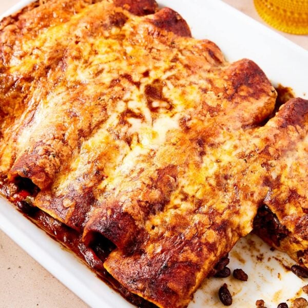 White baking dish filled with baked beef enchiladas with two slices missing with cheese all over the top.