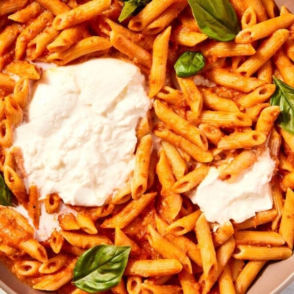 Roasted tomato pasta sitting in large brown bowl with balls of burrata cheese and fresh basil leaves.