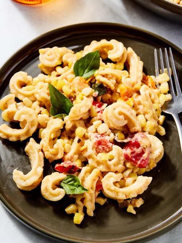 Brown plate on concrete surface filled with sweet corn pasta with glass to the side and more pasta in a bowl behind.