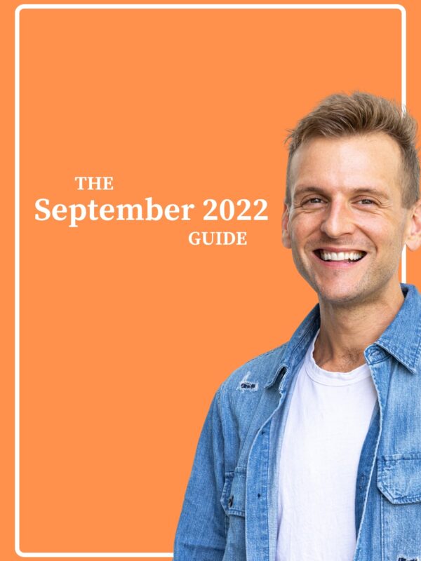 Kaleb Wyse wearing a blue denim shirt over a white shirt standing in front of bright orange background.
