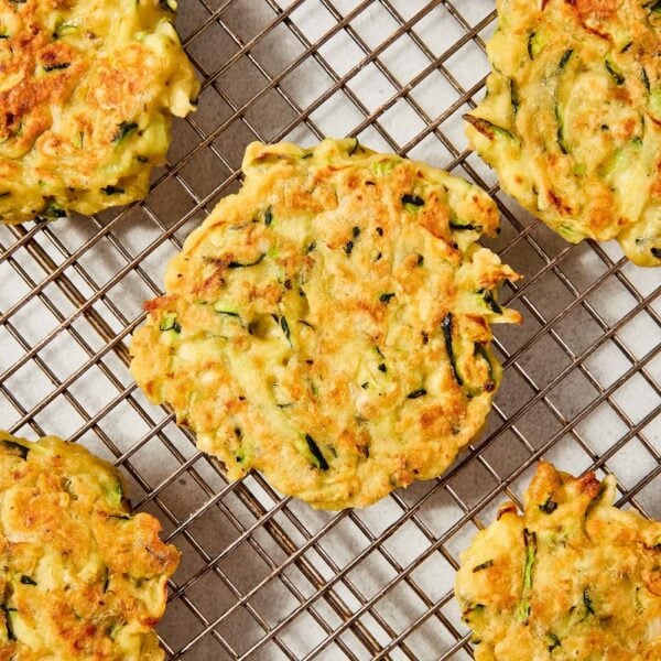 Cooked zucchini fritters sitting on wire cooling rack after being browned on the stovetop.