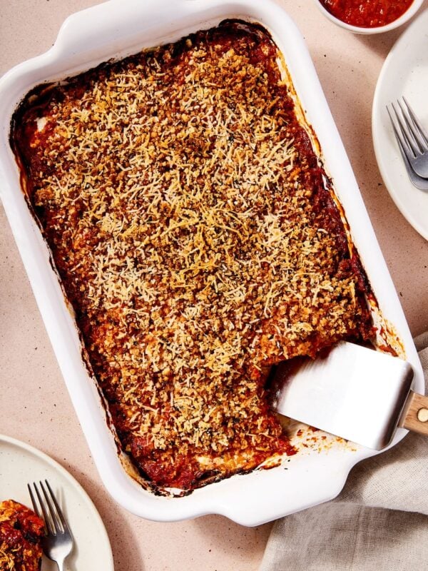 Rectangular white baking dish filled with baked zucchini parmesan with an offset spatula resting on bottom of dish.