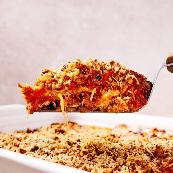 Offset spatula holding serving of zucchini parmesan showing interior layers with rest of casserole below.