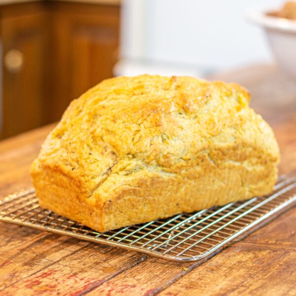 A loaf of bread sits on a cooling rack on a wooden kitchen island.