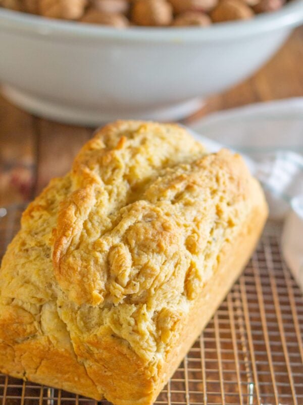 A loaf of bread sits on a cooling rack on a wooden table.