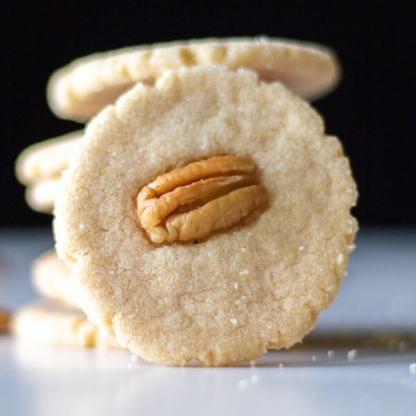 A cookie with a pecan in the center leans against a stack of cookies.