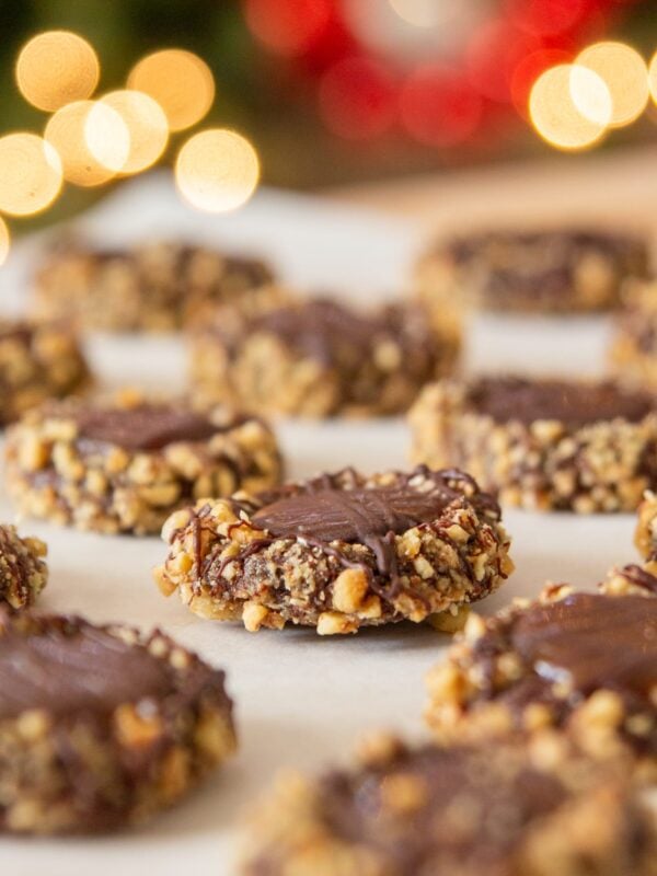 Cookies lined in rows sit on parchment paper in front of Christmas lights.