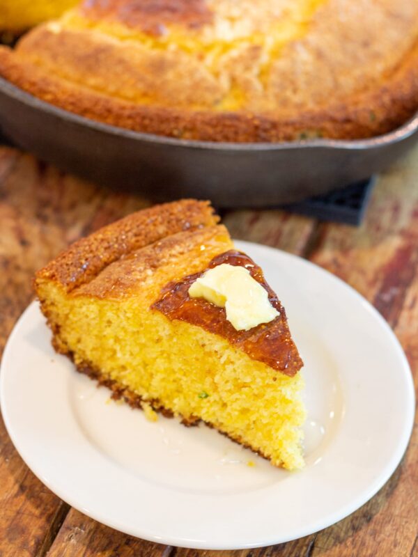 A slice of cornbread topped with butter sits on a plate.