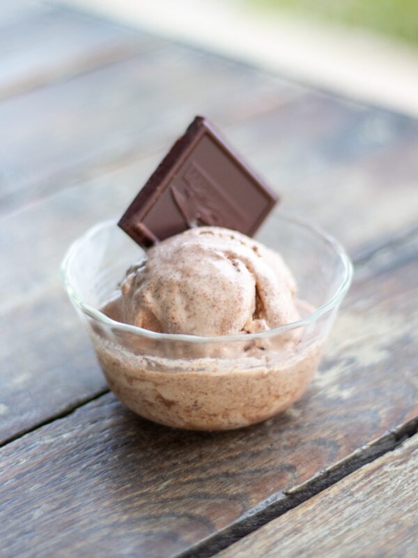 A scoop of chocolate ice cream sits in a bowl on a table outside.