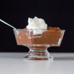 Chocolate pudding topped with whipped cream sits in a glass dish.