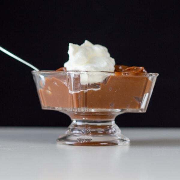 Chocolate pudding topped with whipped cream sits in a glass dish.