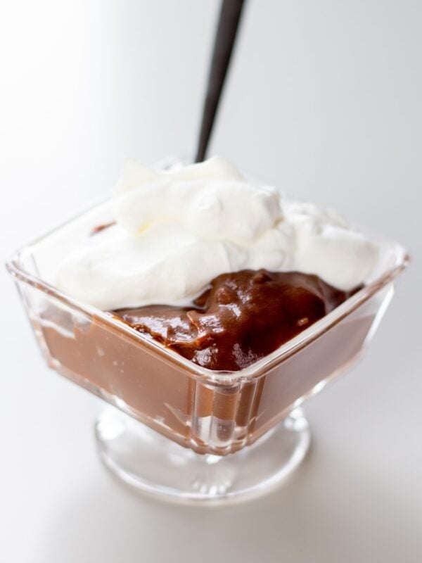 Chocolate pudding with whipped cream sits in a glass container.