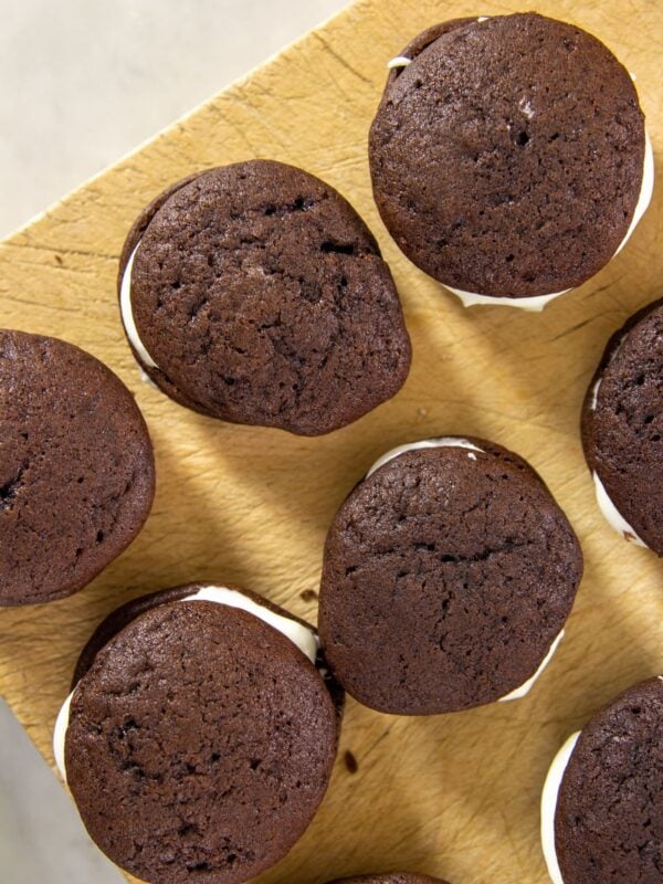 Chocolate cookies filled with marshmallow cream lie flat on a wooden block.