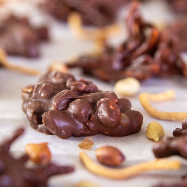 A peanut cluster dipped in chocolate sits on parchment paper.