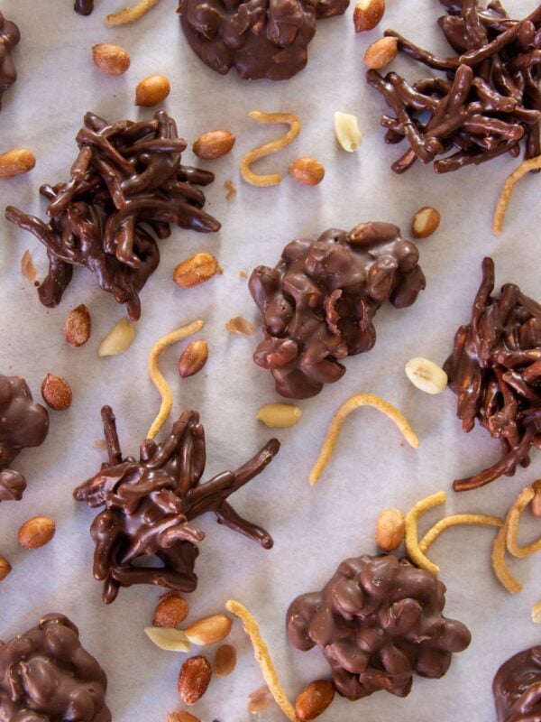 Peanut clusters and chow mein dipped in chocolate are scattered across parchment paper.