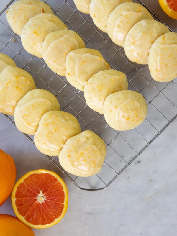 Cookies sit on a cooling rack next to oranges.
