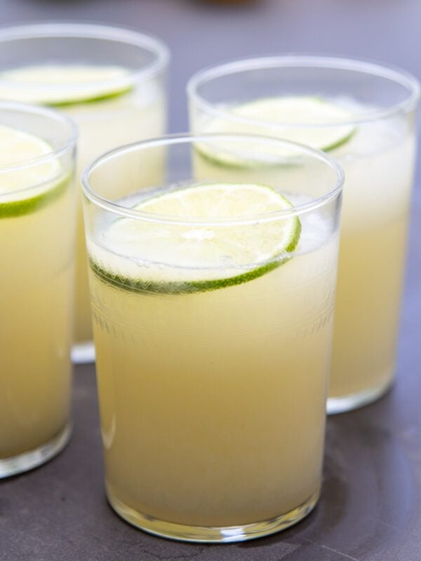 A glass full of lemonade sits on a table next to other glasses.