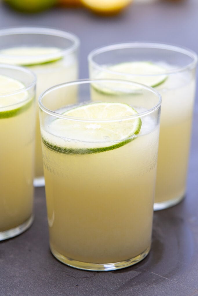 A glass full of lemonade sits on a table next to other glasses.