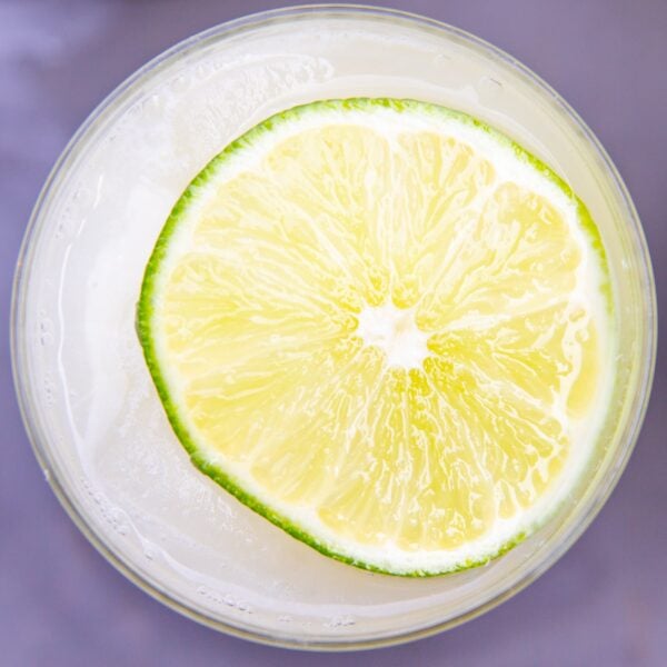 A slice of lime floats on top of a glass full of lemonade.