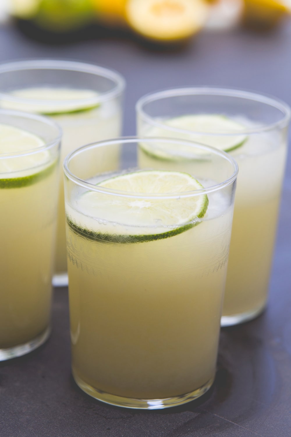 A glass full of lemonade topped with a lime sits on an outdoor table.