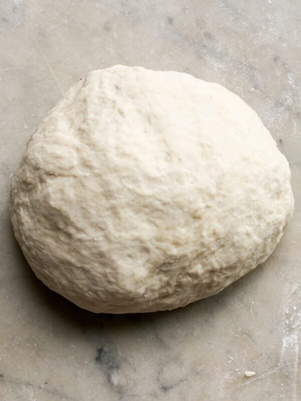 A ball of pizza dough rests on a floured surface.