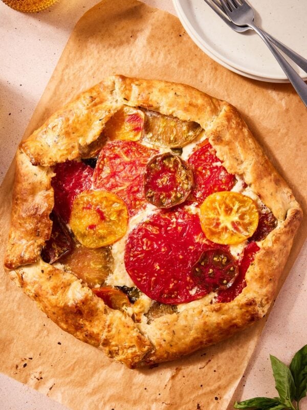 Freshly baked tomato galette resting on a piece of parchment paper with plates sitting to the side.