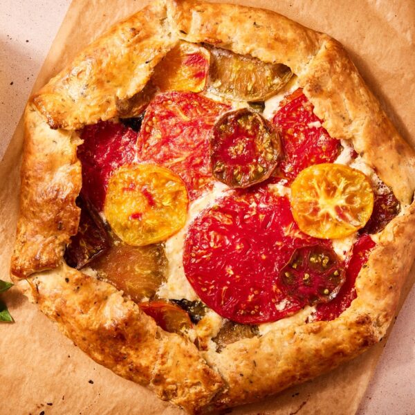 Freshly baked golden brown tomato galette sitting on piece of parchment with sprig of fresh basil.