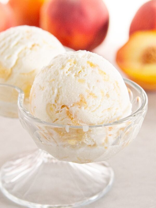 A scoop of peach frozen yogurt sits in front of peaches.
