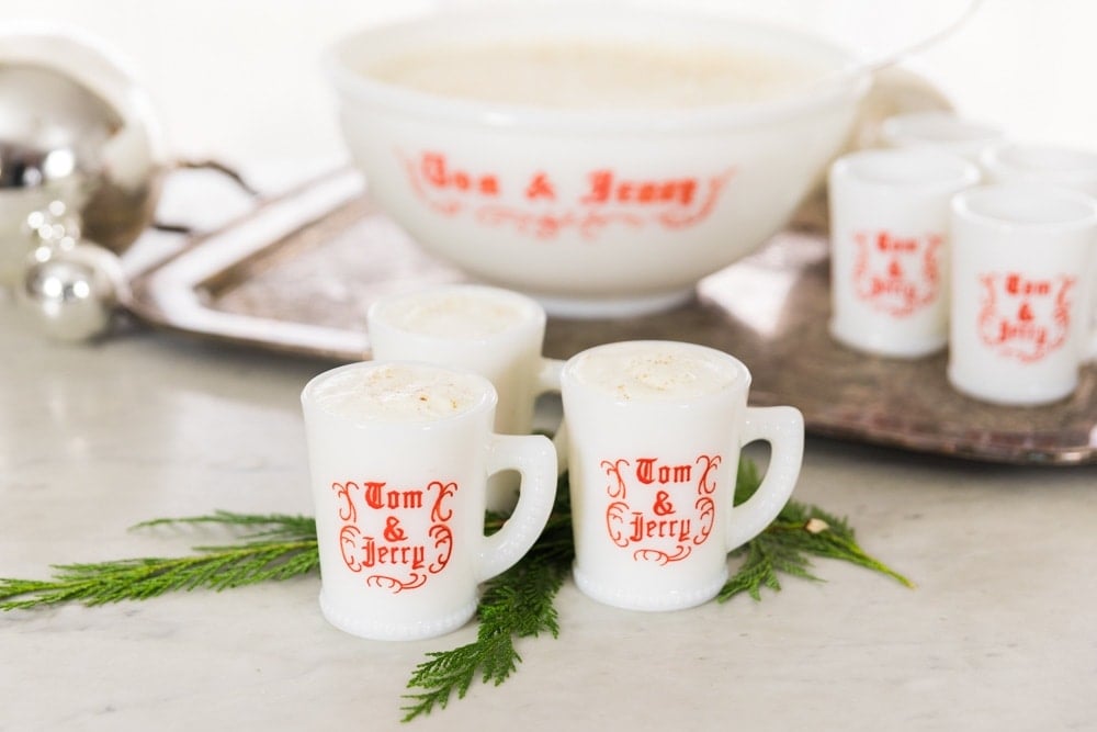 Mugs full of eggnog sit in front of a serving bowl.