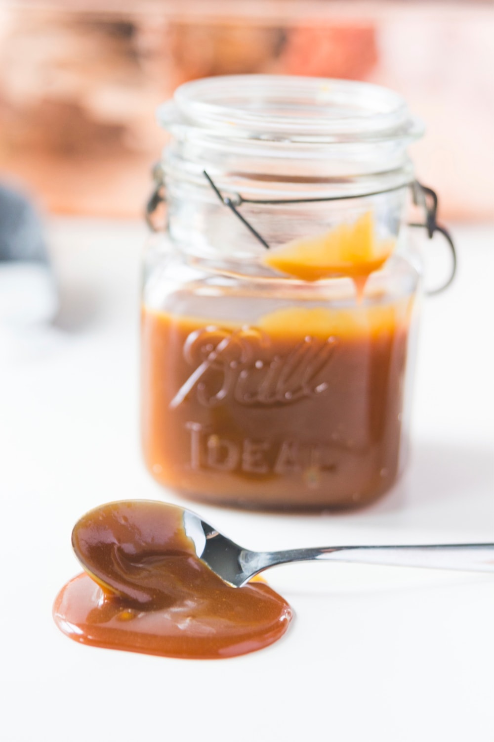 A spoon drips caramel onto a table in front of a full jar.