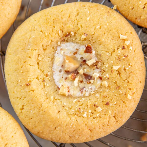 A cookie topped with honey butter and almond pieces rests on a cooling rack.