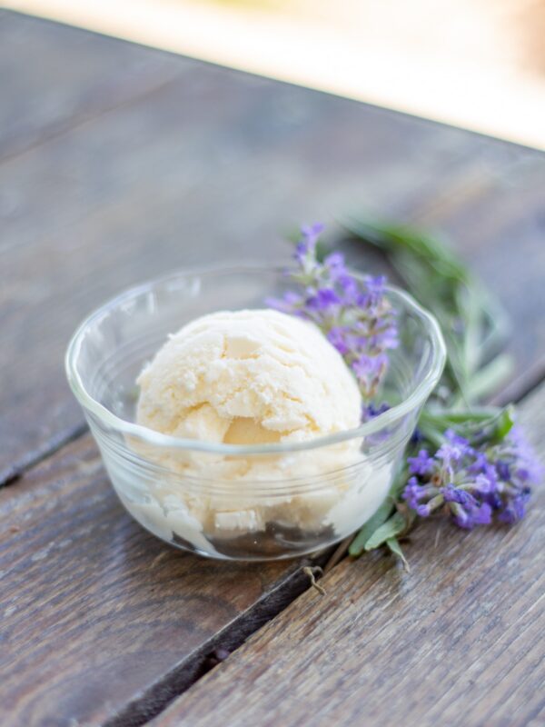 A scoop of ice cream sits in a dish next to lavender.