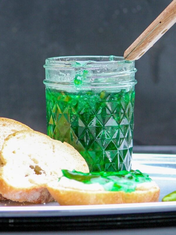 Jelly spread on a bread in front of a jar.