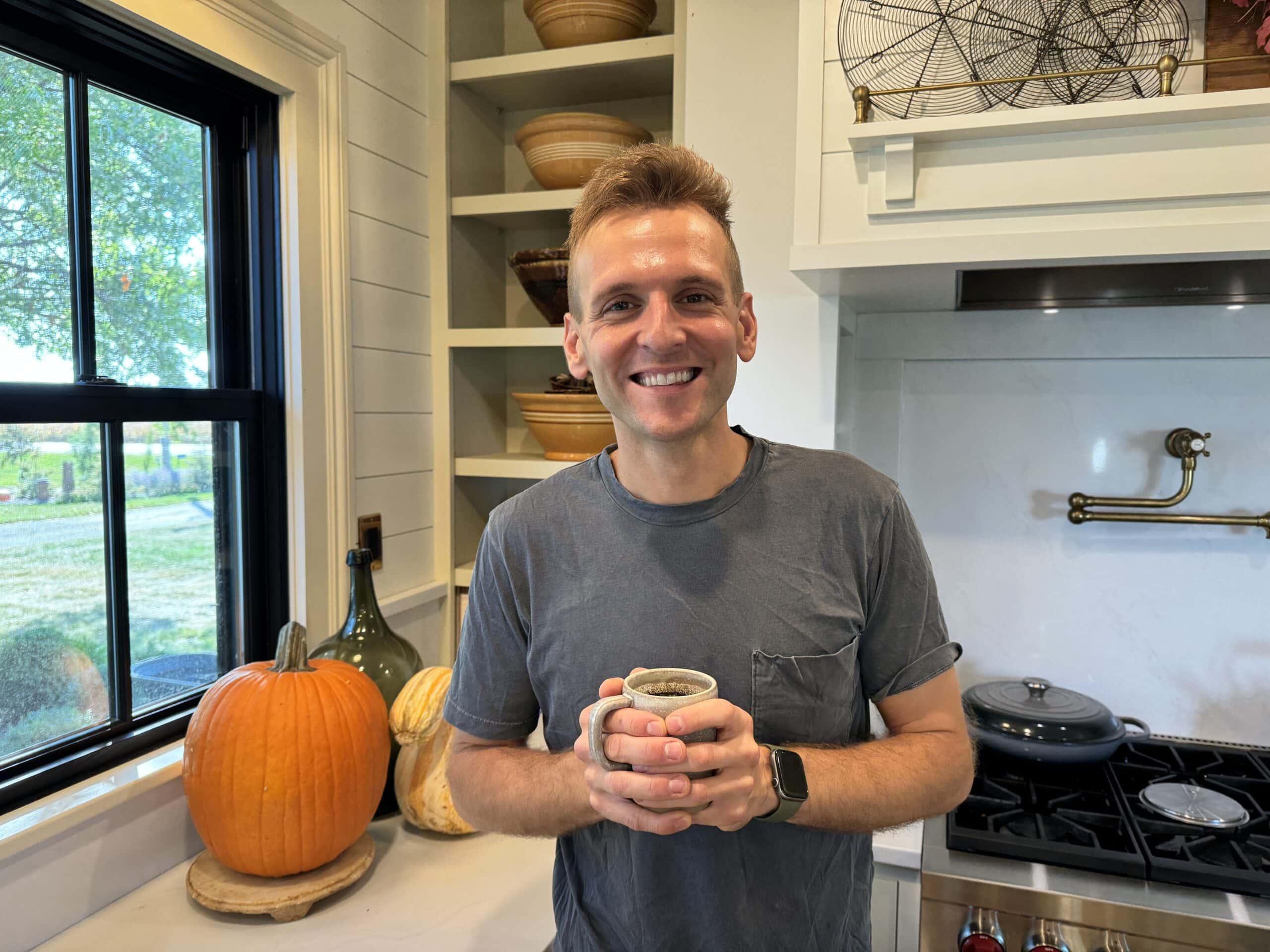 Kaleb Wyse standing in kitchen holding a glass of hot coffee with pumpkin in the background.