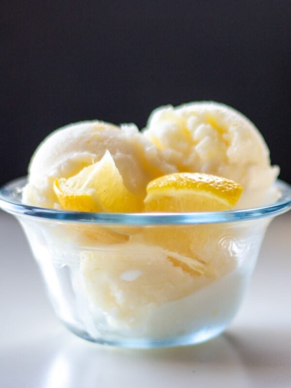 Two scoops of ice cream sit with lemon slices in a glass dish.
