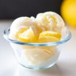 Two scoops of ice cream sit with lemon slices in a glass container.