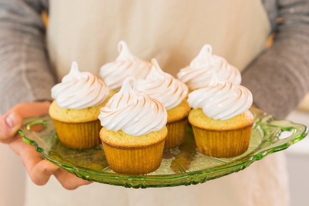 A person holding a platter of cupcakes with meringue frosting.
