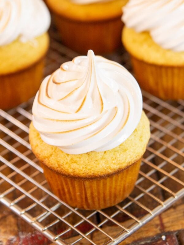 A cupcake with twirled frosting sits on a cooling rack.