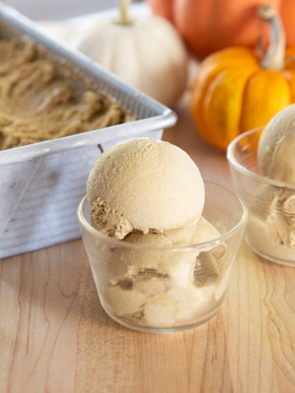 Scoops of ice cream sit in a dish in front of small pumpkins.