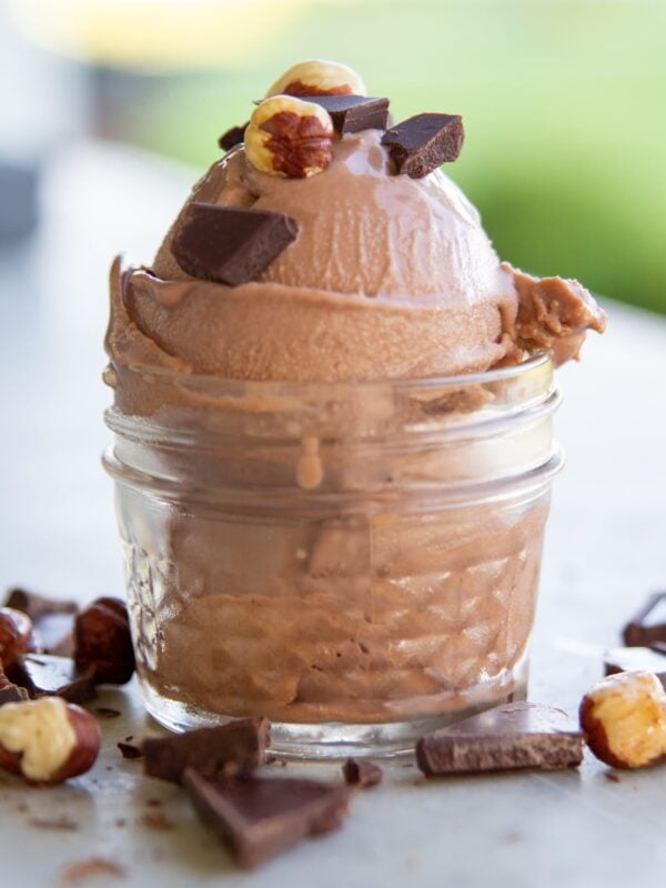 Hazelnut and chocolate adorn a scoop of ice cream in a dish.