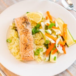 Salmon sits on a bed of rice next to vegetables.