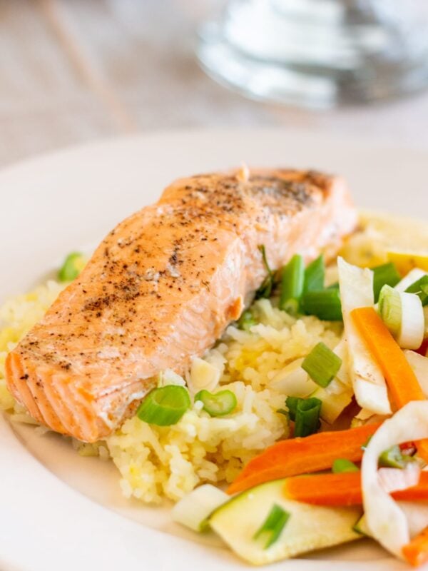 Salmon sits on a bed of rice next to vegetables.