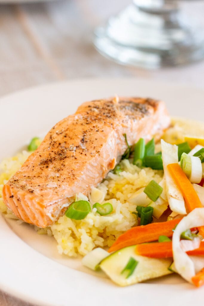 Salmon sits on a bed of rice next to vegetables.