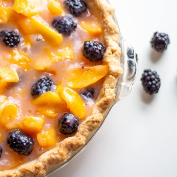 A pie with peach and blackberries sits next to blackberries.