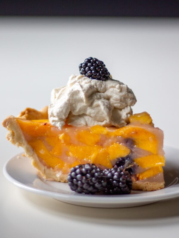 A slice of peach and blackberry pie sits on a plate.