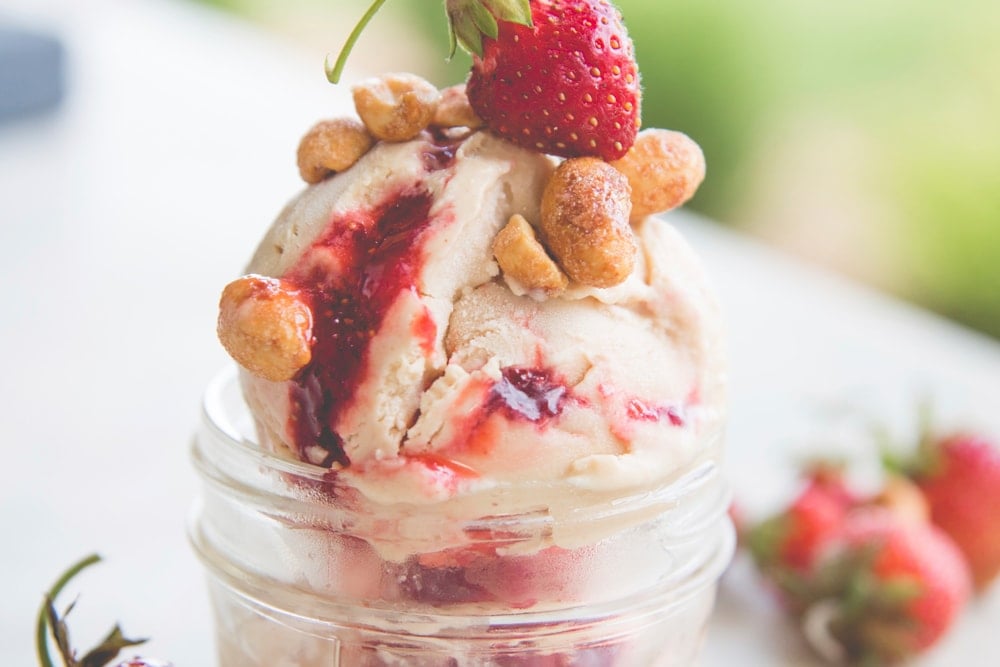 A scoop of ice cream topped with nuts and a strawberry.